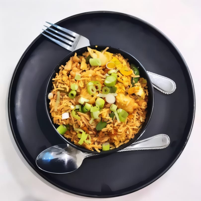 Indian fried rice with chicken and vegetables, garnished with green onions, served on a black plate.